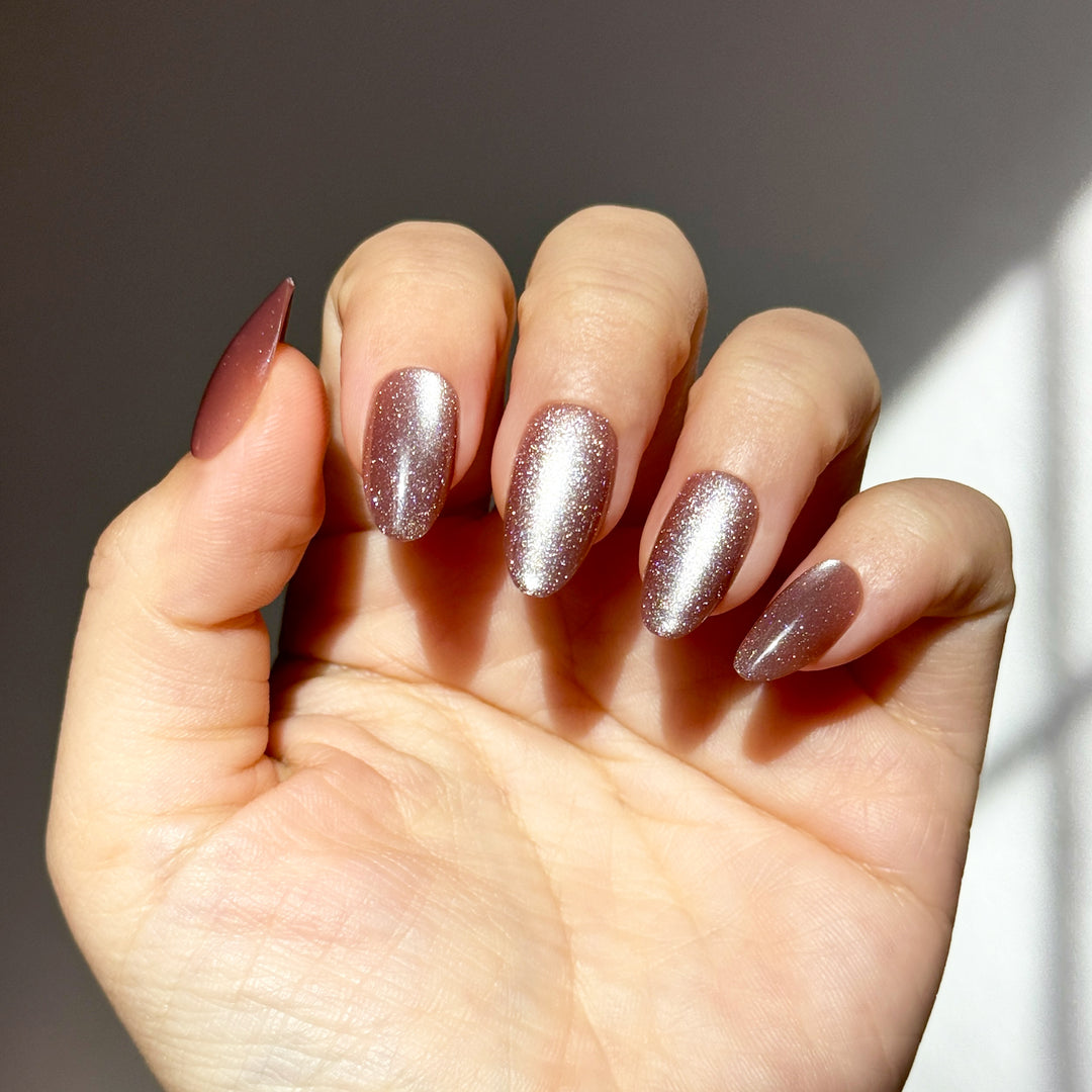 Medium almond-shaped press-on nails with a metallic cat-eye finish. The color is a dusty rose mauve with a bright, silvery magnetic stripe reflecting light vertically down the center of each nail.