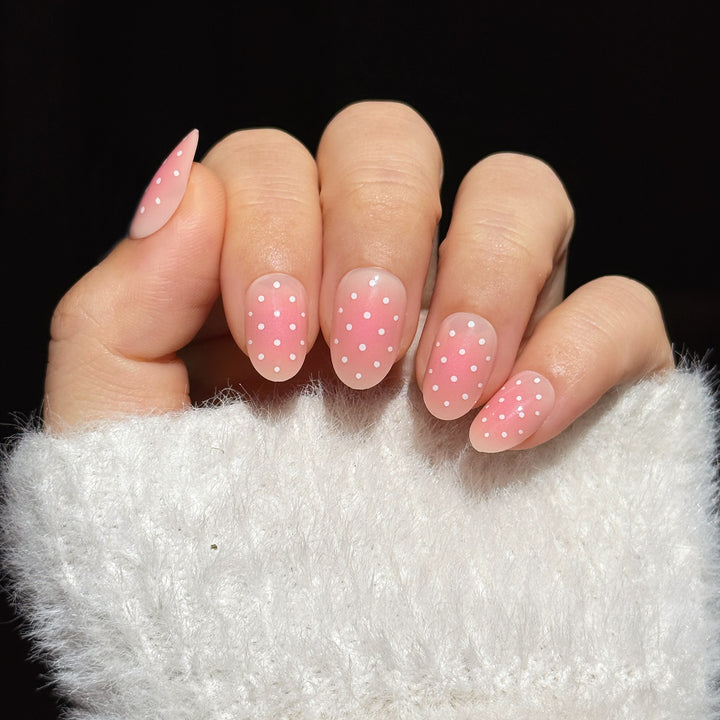 Press on nails hand model with pink ombre design featuring white polka dots.