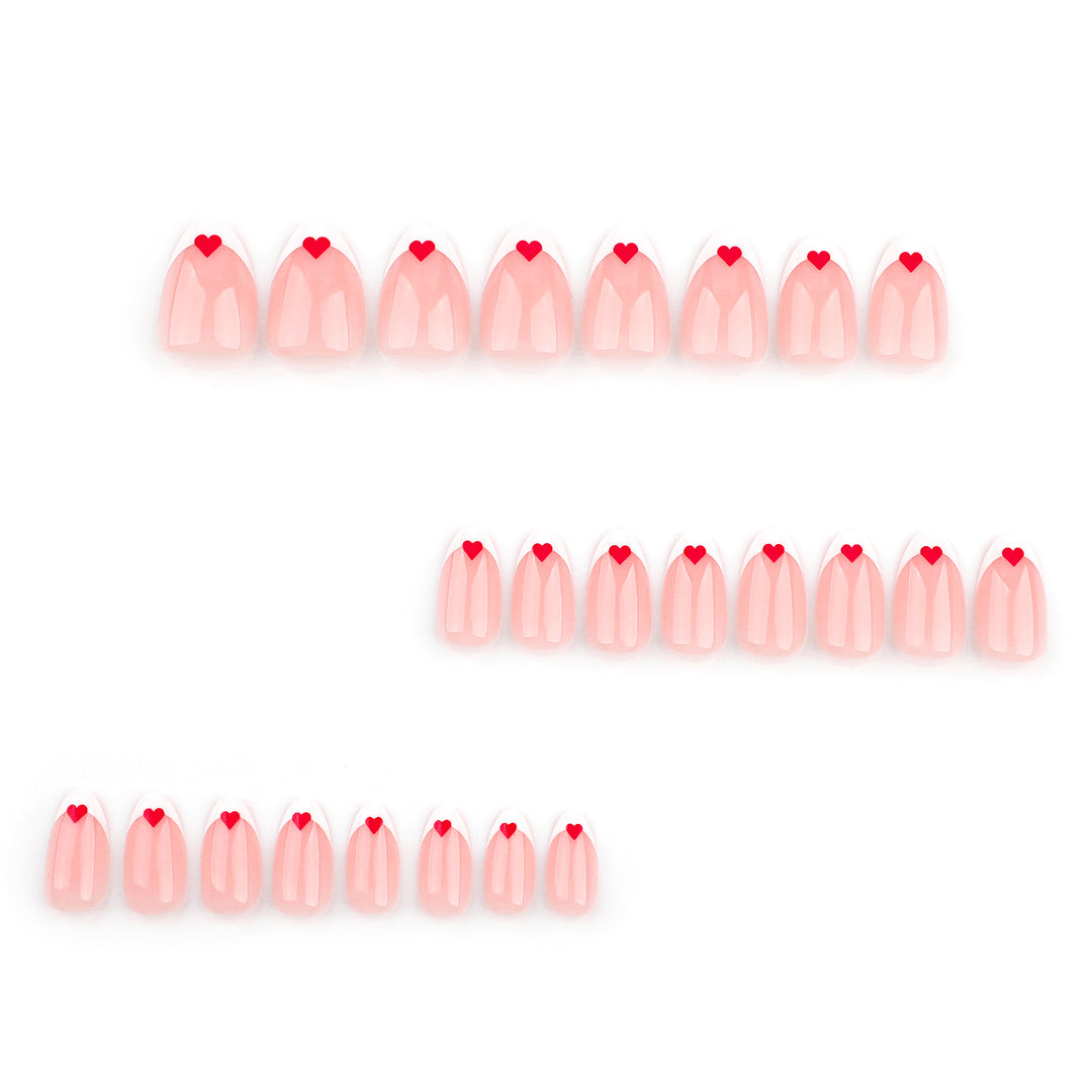 A set of 24 press-on nails in a soft almond shape displayed on a white background. The nails feature a sheer milky pink base with a classic white French tip and a small, vibrant red heart detail centered at the top of each white tip.