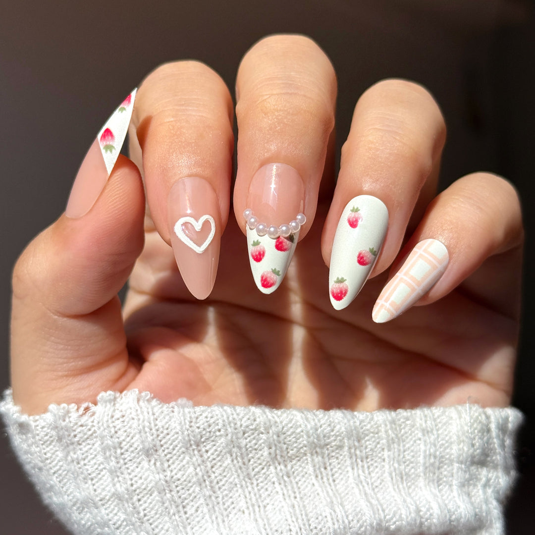 Almond-shaped press-on nails featuring a mix of shimmering white marble texture and natural-base French tips with small red cherry illustrations on the tips.