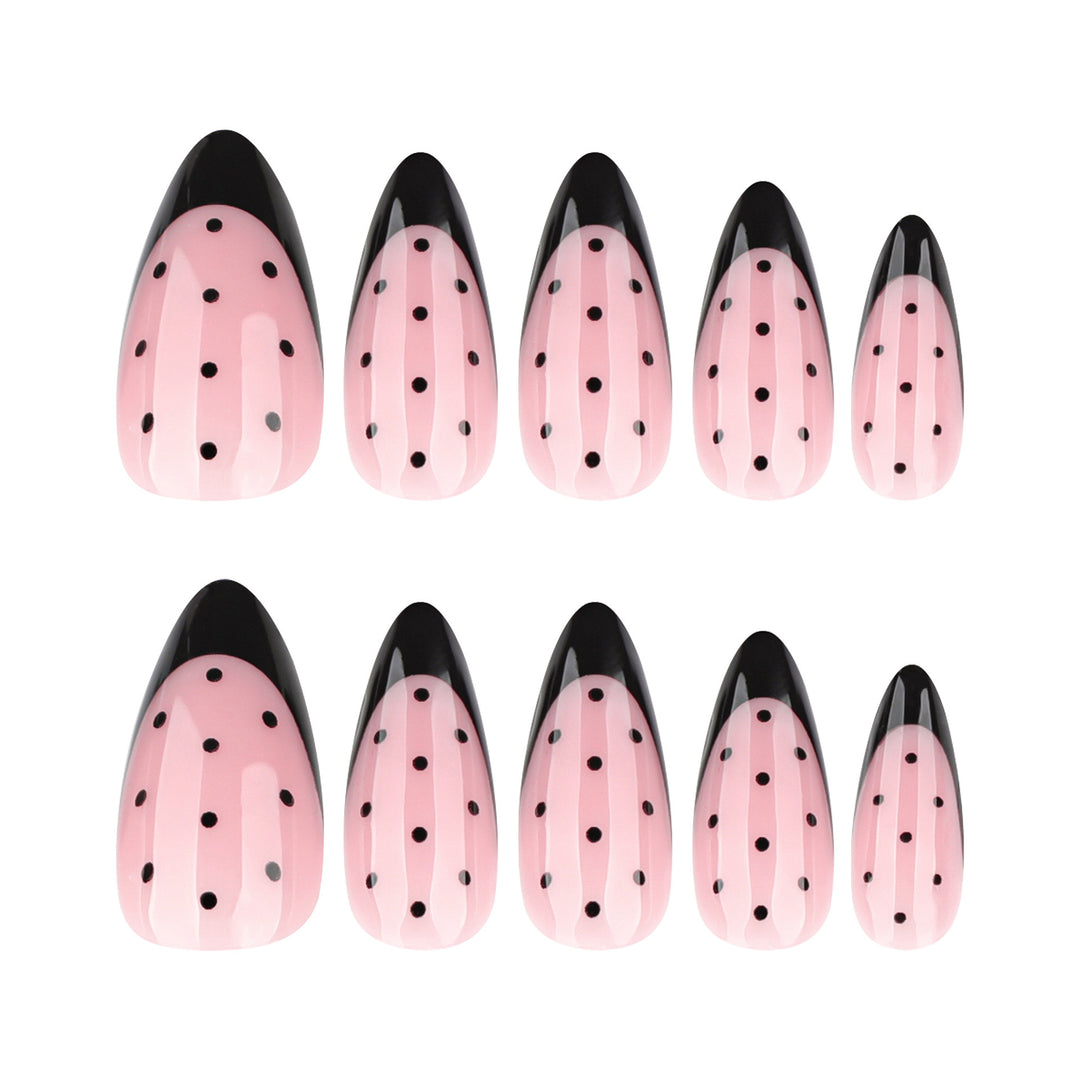 Almond-shaped press-on nails with a soft pink base, black French tips, and black polka dot nail art.