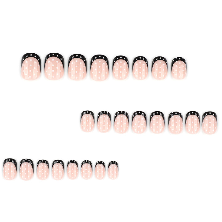 The design features a nude base with black French tips and a consistent white polka dot pattern across the entire nail.