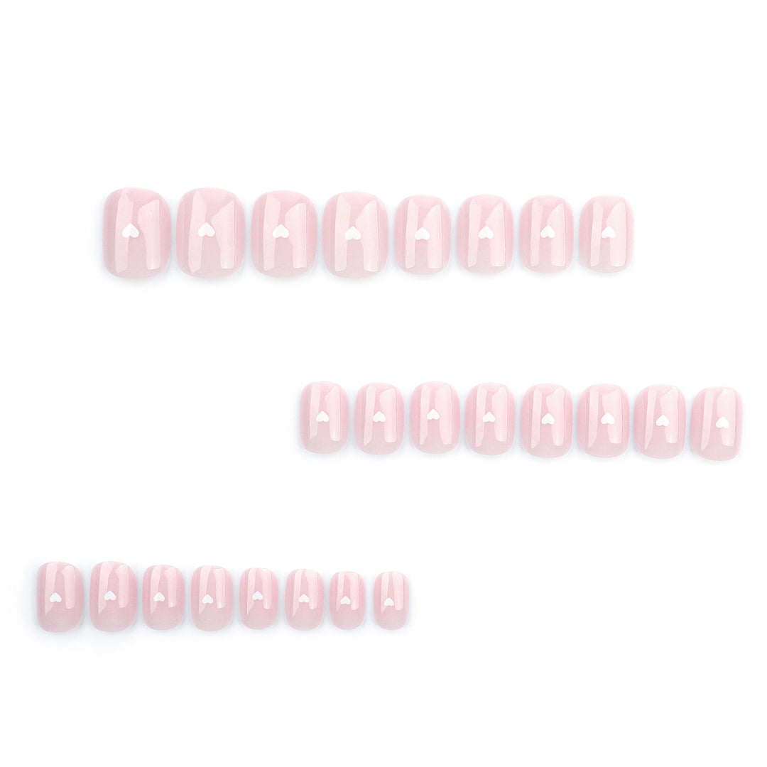 A set of short, square-round press-on nails in a sheer, milky pale pink. Each nail features a small, white 3D heart centered in the middle of the nail bed. The finish is high-gloss, and the overall look is clean, minimalist, and soft.