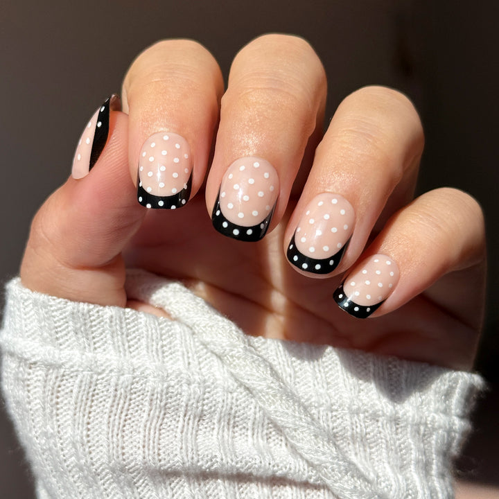 Hand with polka dot nail design on a dark background