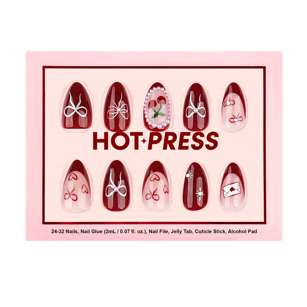 Almond press-on nails with dark red and clear designs. Features include small white and red bows, tiny red hearts, and a special accent nail with two red cherries inside a white pearl frame. The package includes 24-32 nails, glue, a file, jelly tabs, a cuticle stick, and an alcohol pad.